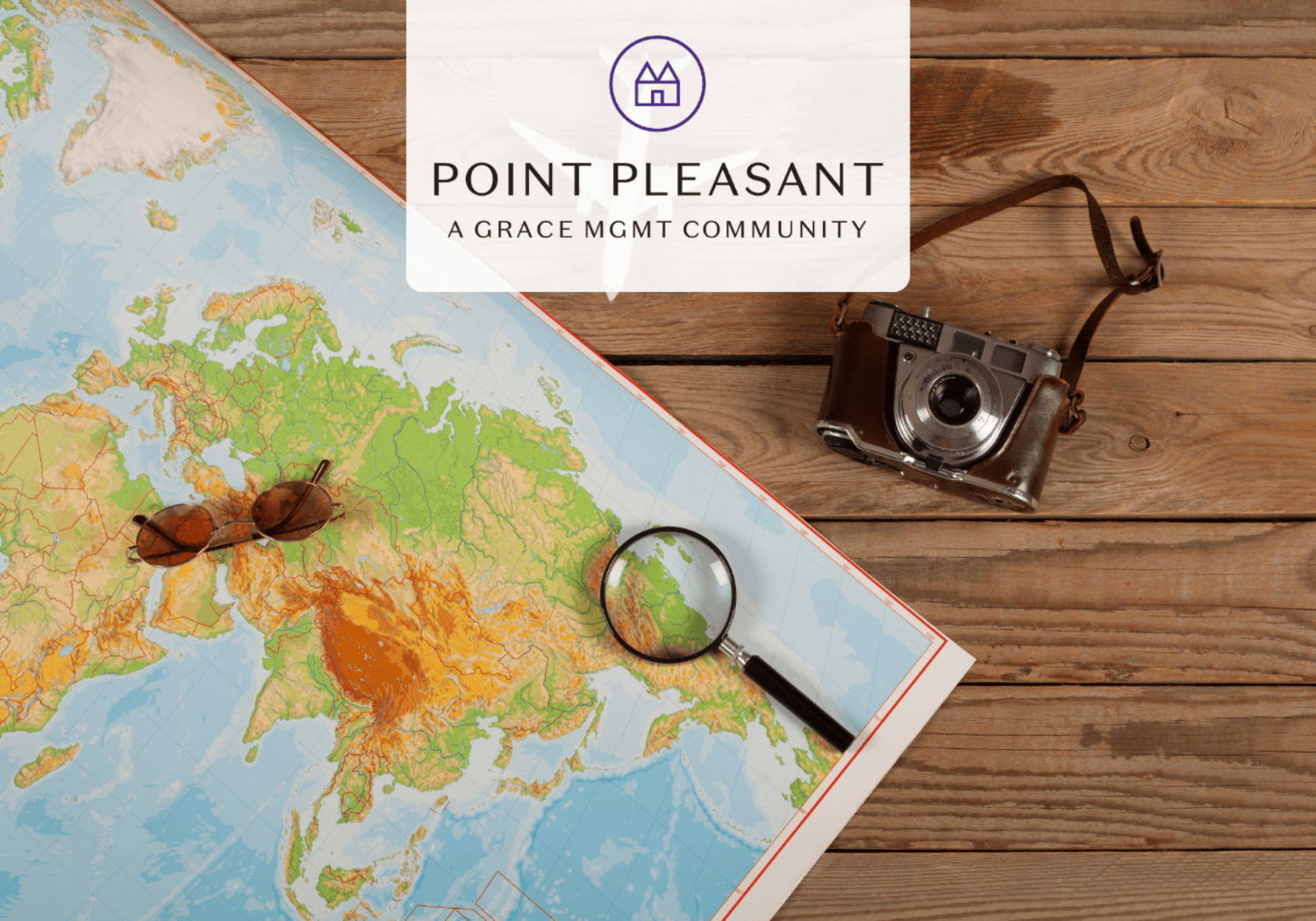 Travel planning scene with a map, camera, magnifying glass and sunglasses on a wooden table, featuring a translucent logo reading Point Pleasant A Grace Mgmt Community.