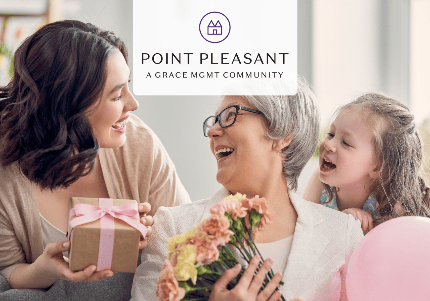 Three generations sharing a joyful moment indoors, with flowers and a gift, for Point Pleasant community.