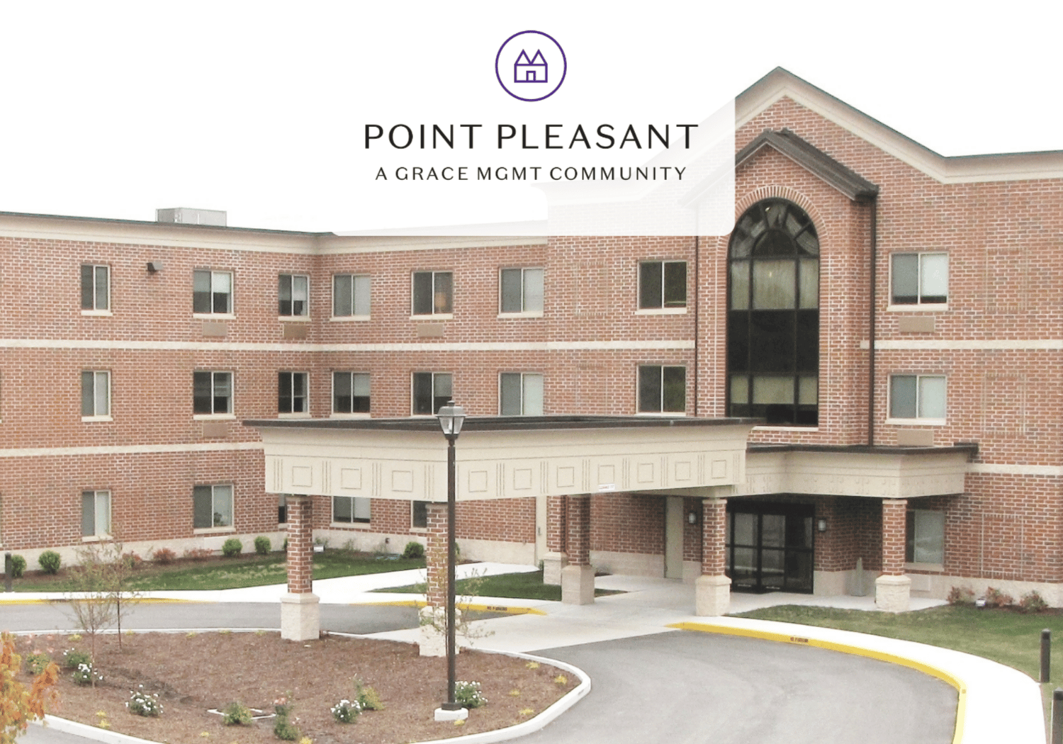 Exterior view of Point Pleasant, a Grace Mgmt Community, with brick building, covered entrance, and circular purple logo at the top center of the image.