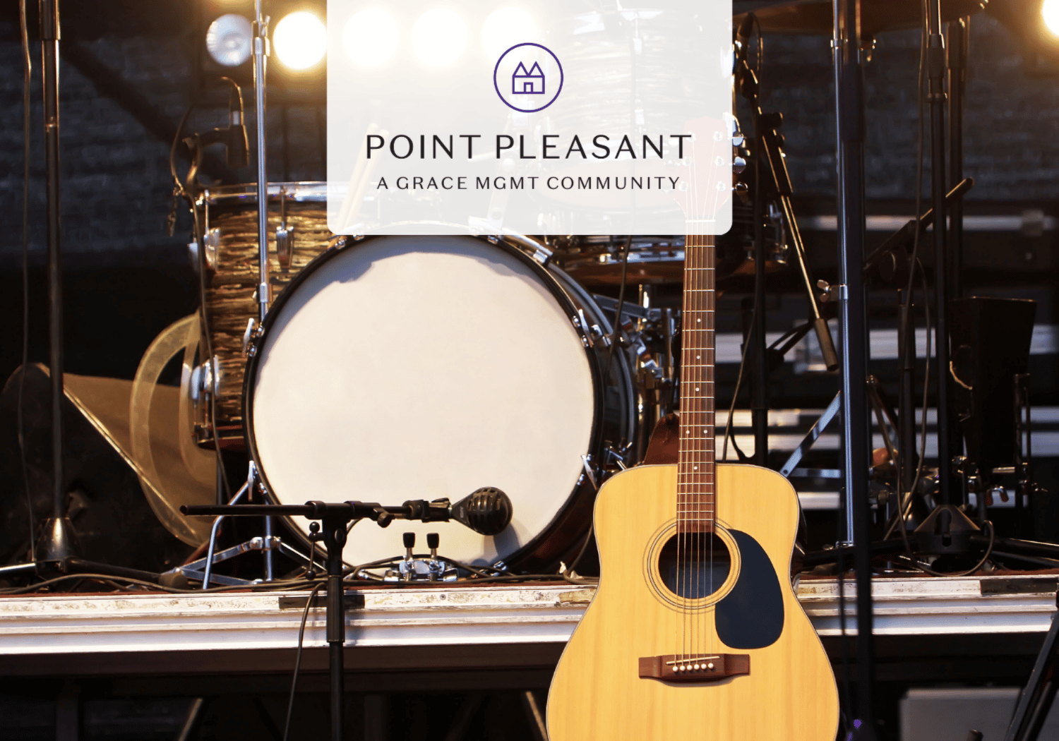 Acoustic guitar on a stage in front of a drum kit, with a translucent banner reading 'Point Pleasant A Grace Mgmt Community'.